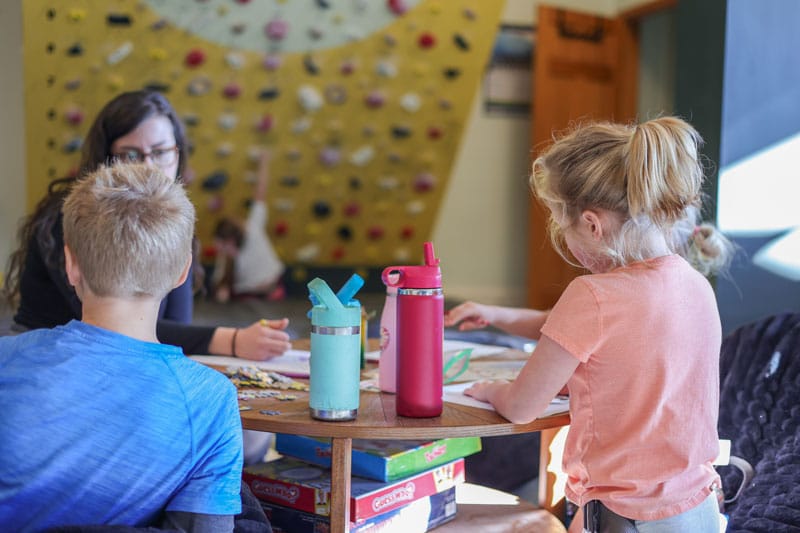 Children work with an instructor on activities like coloring and games at rock climbing camp